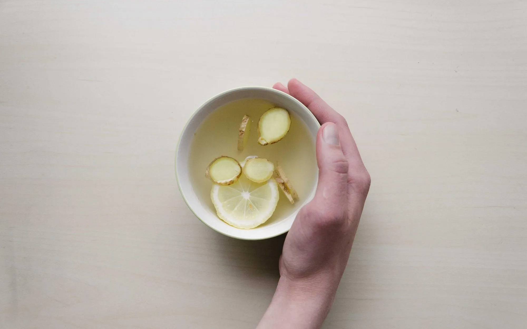 Hands cradling a small white bowl of clear broth with dumplings