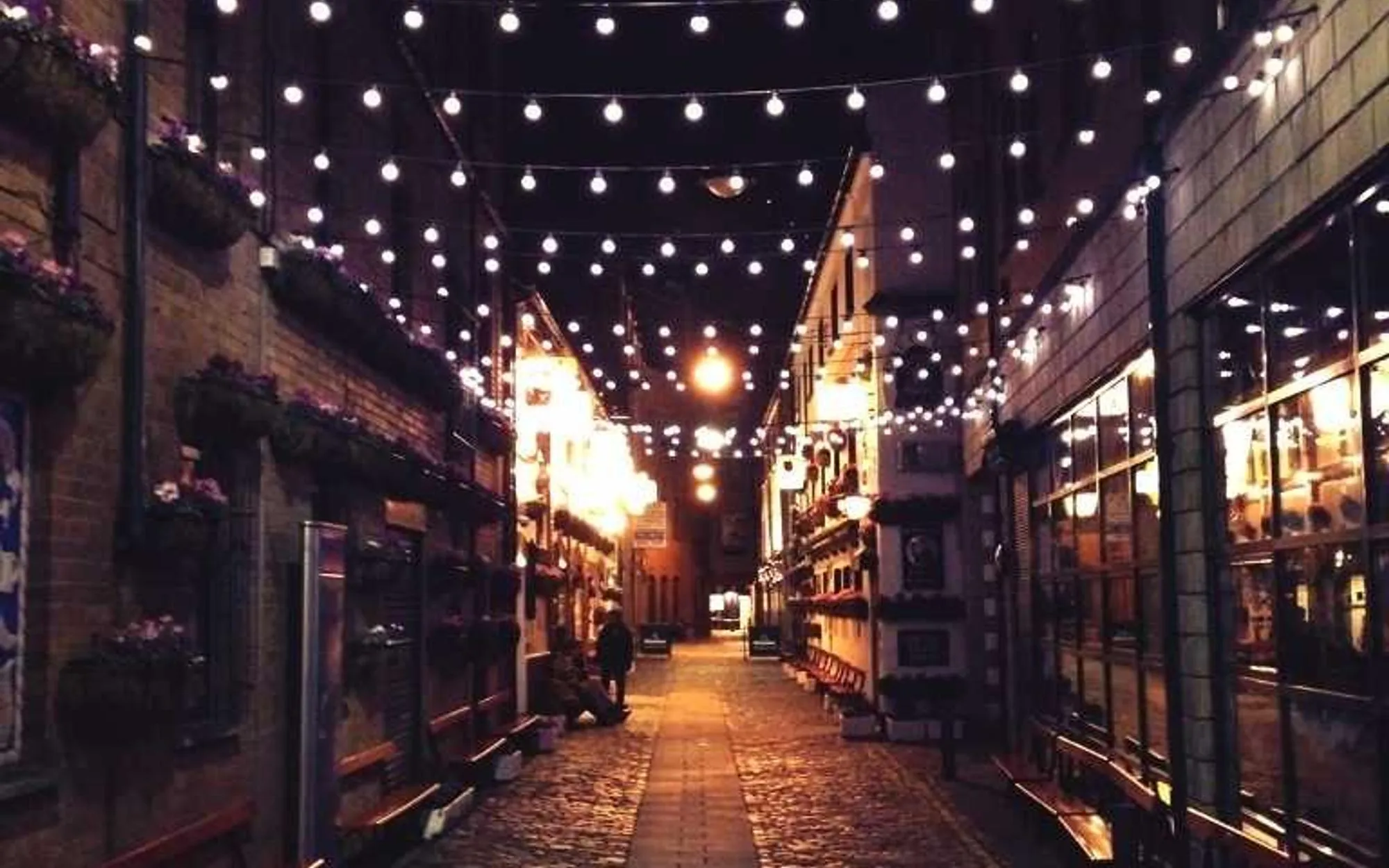 A narrow market street at night strung with warm festoon lights