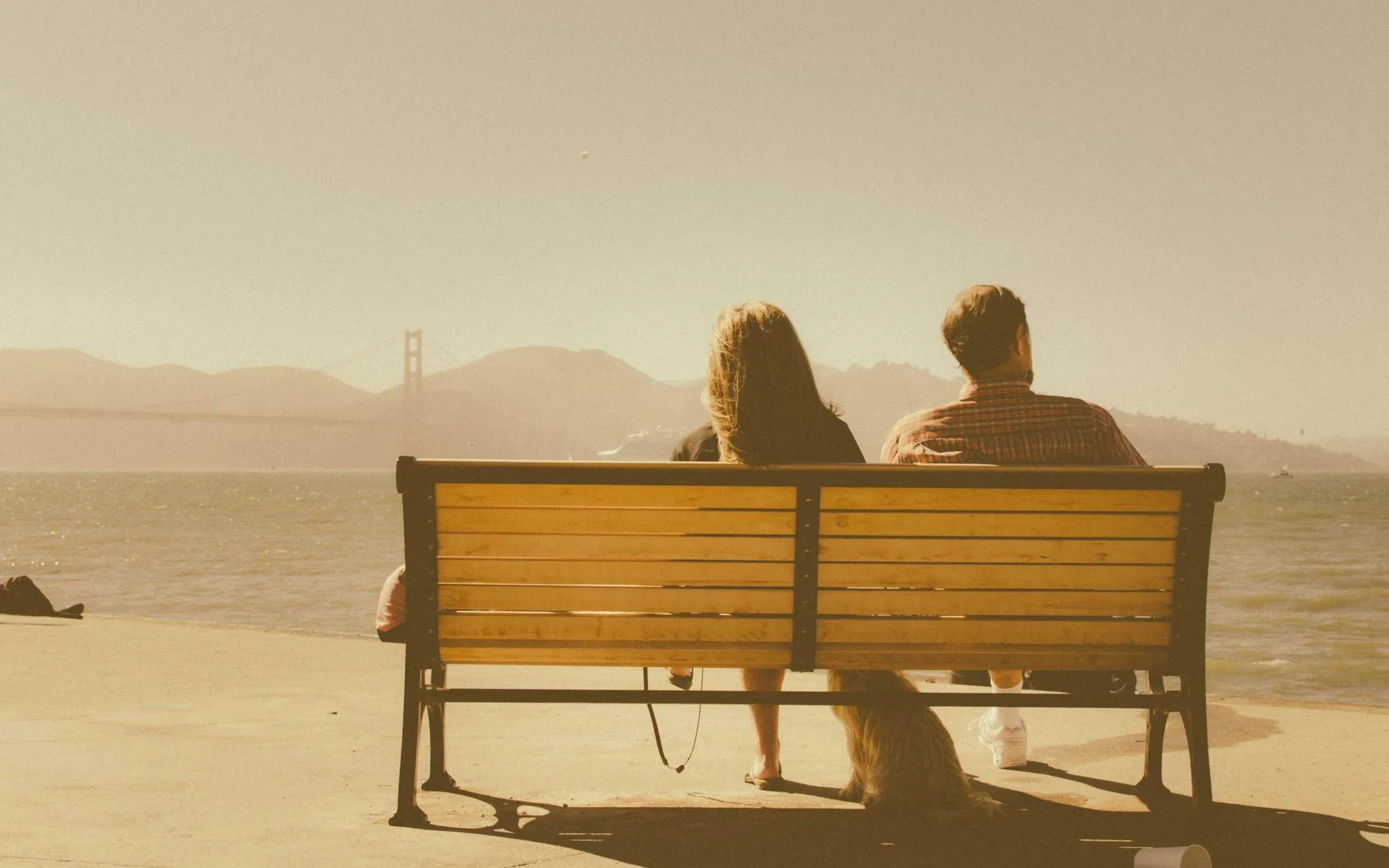 Two people sitting on a bench looking out over water at sunset