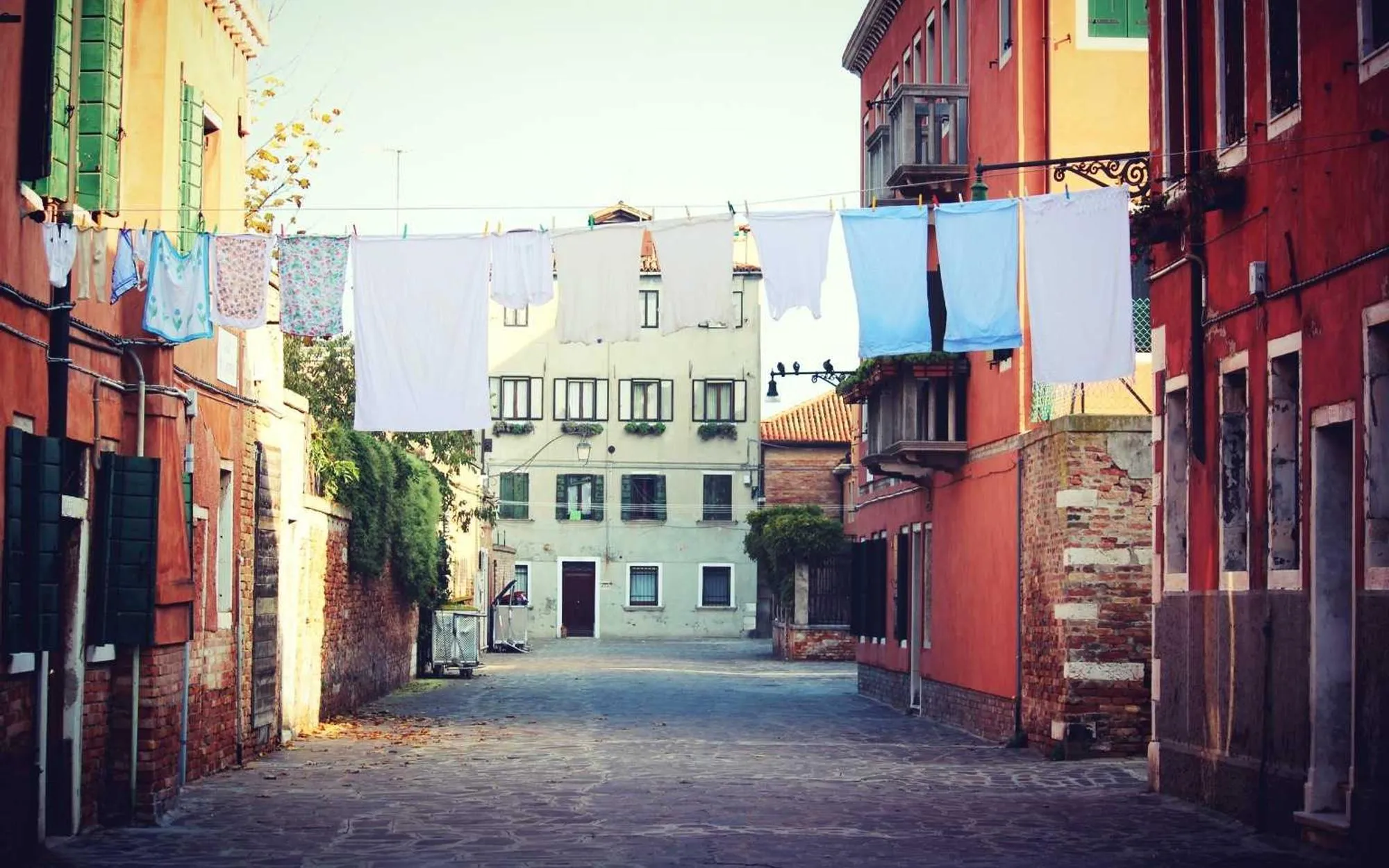 A narrow canal in Burano lined with houses painted pink, orange and blue